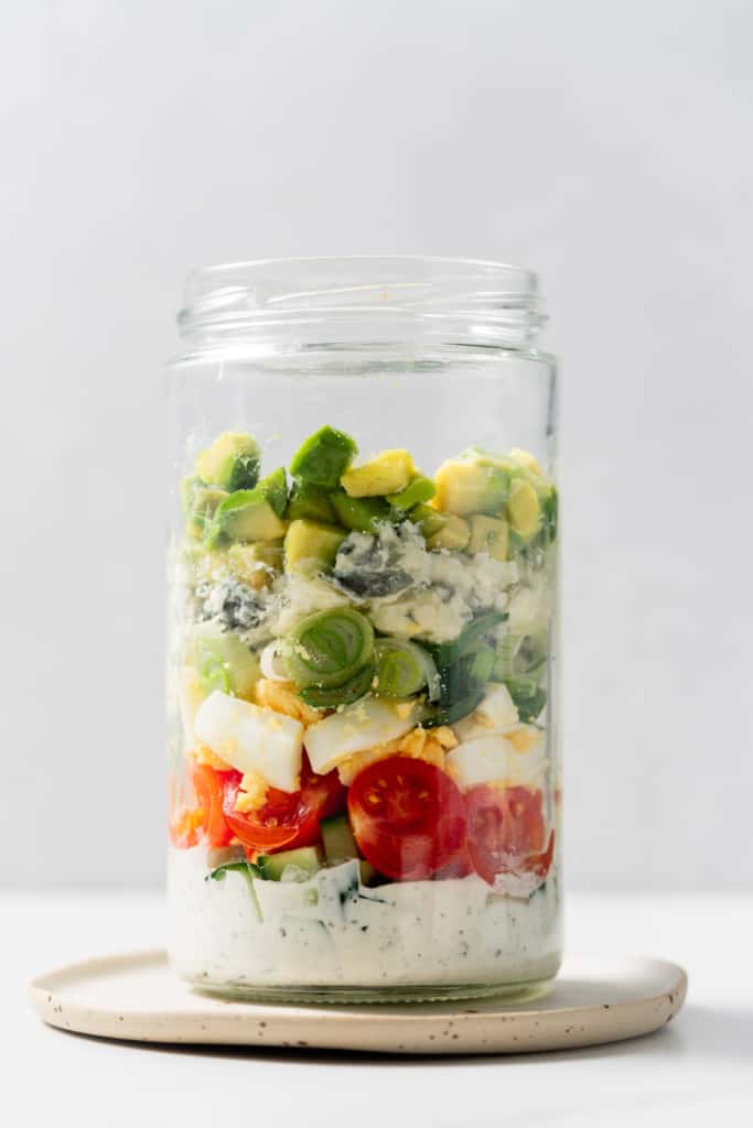 Filling a glass jar with tomatoes, cheese and avocado.