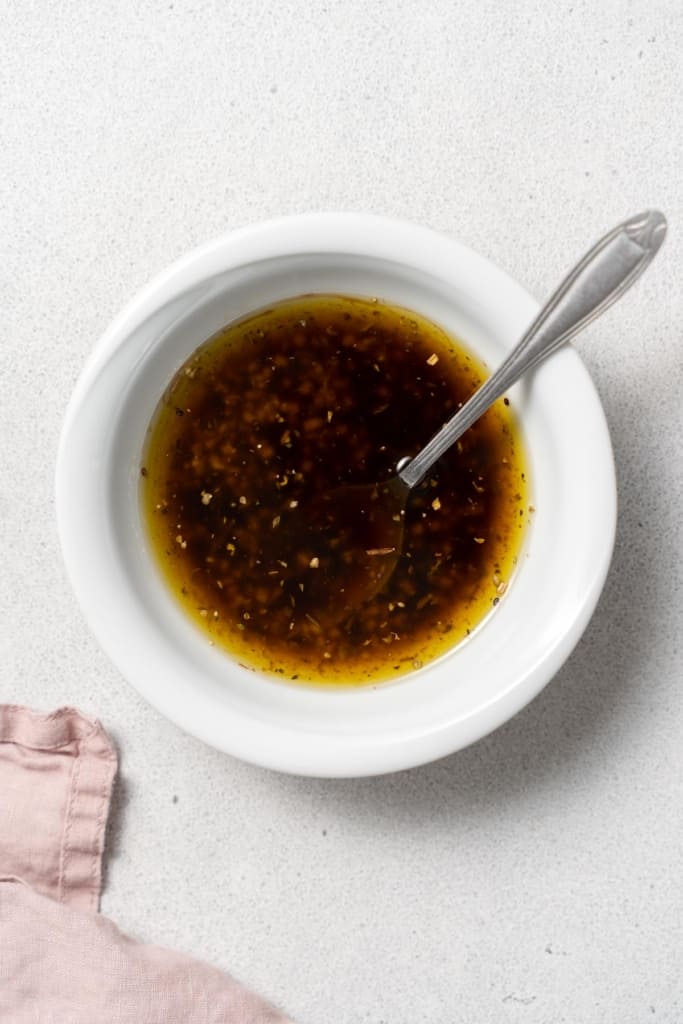 Stirring together vinaigrette in a small white bowl.
