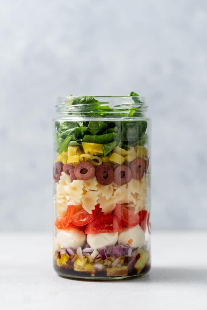 Topping a salad jar with banana peppers and spinach.