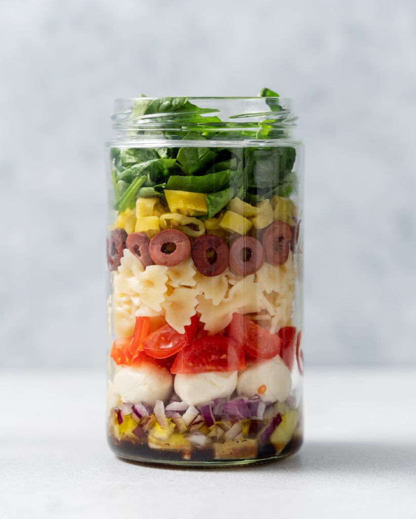 Topping a salad jar with banana peppers and spinach.
