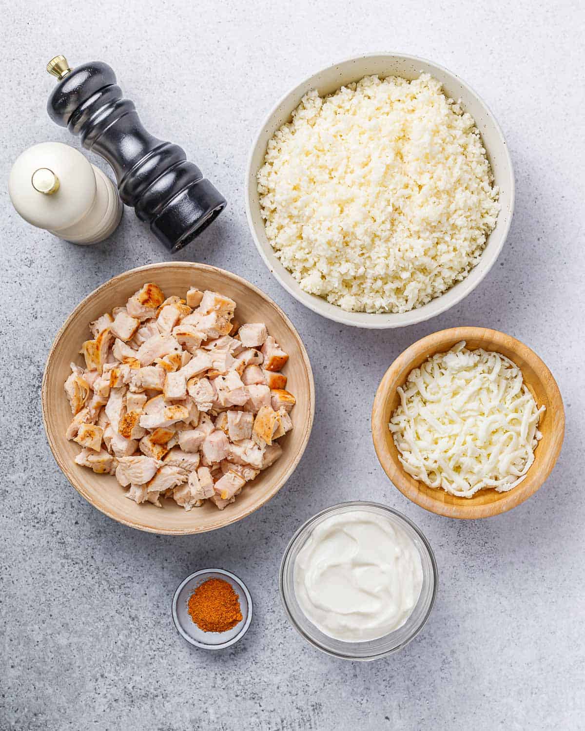 Chopped chicken, cauliflower rice, cheese and sour cream divided into small bowls.