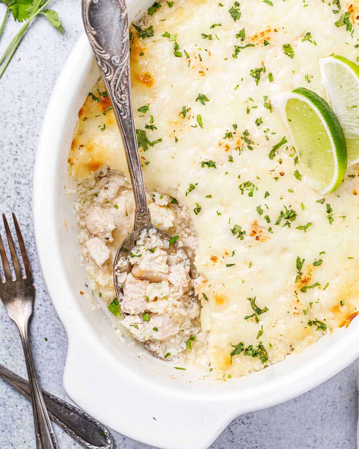 Spoon serving chicken cauliflower rice casserole out of a white baking dish.