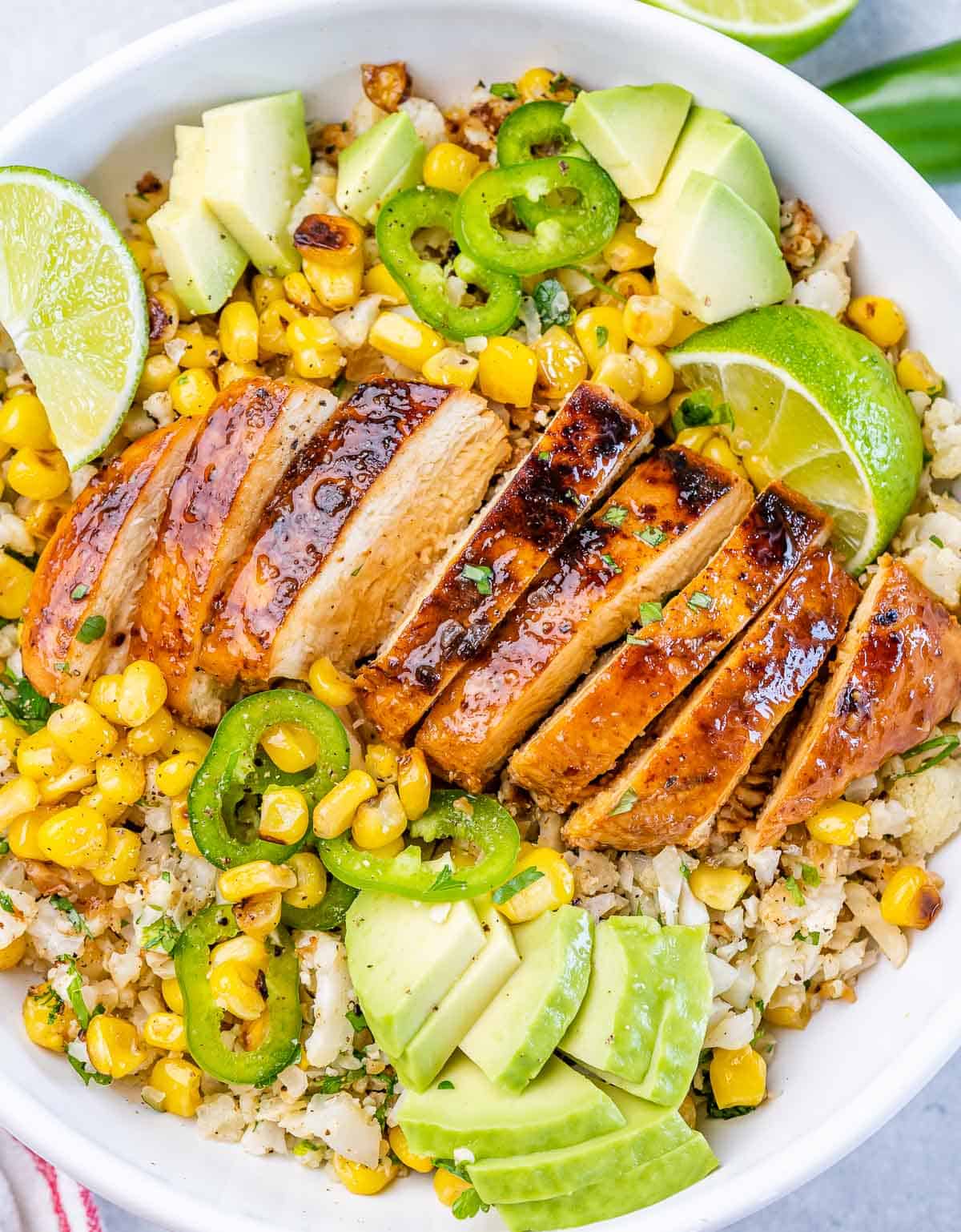 Closeup view of sliced, seared chicken served over cauliflower rice and corn in a bowl.