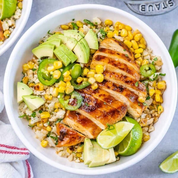 top view bowl with cauliflower rice topped with sliced grilled chicken breast with corn avocado and sliced jalapeno