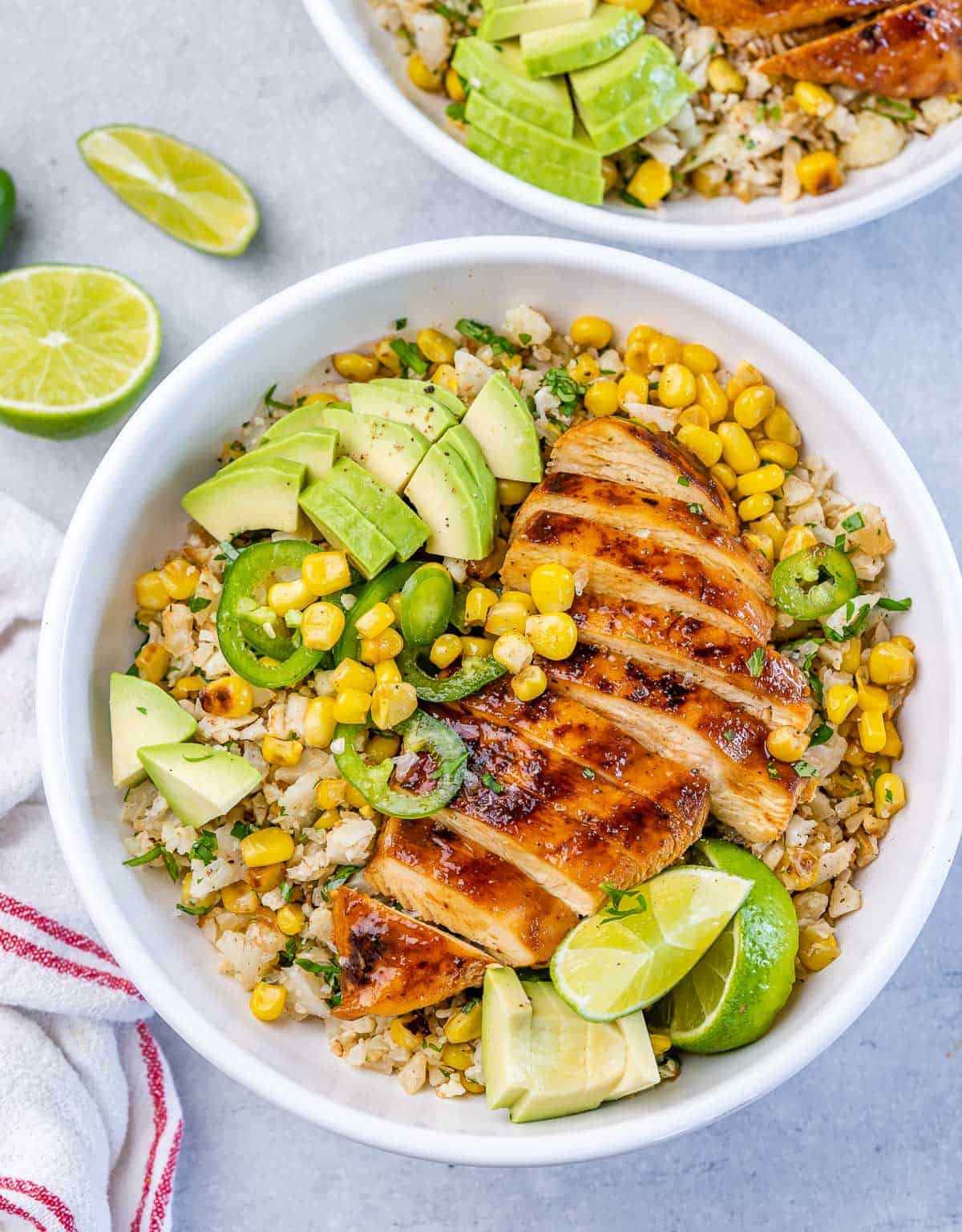Top view bowl with cauliflower rice topped with sliced grilled chicken breast with corn avocado and sliced jalapeño.