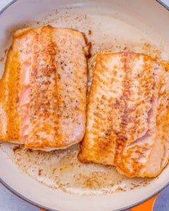 Two salmon filets searing in a skillet until golden brown on the outside.