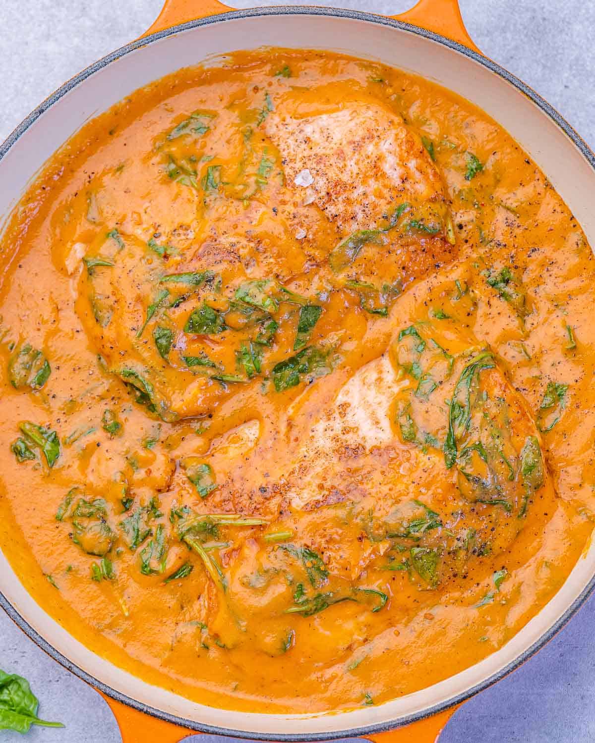 Overhead shot of salmon cooking in a thick spinach and roasted red pepper sauce.