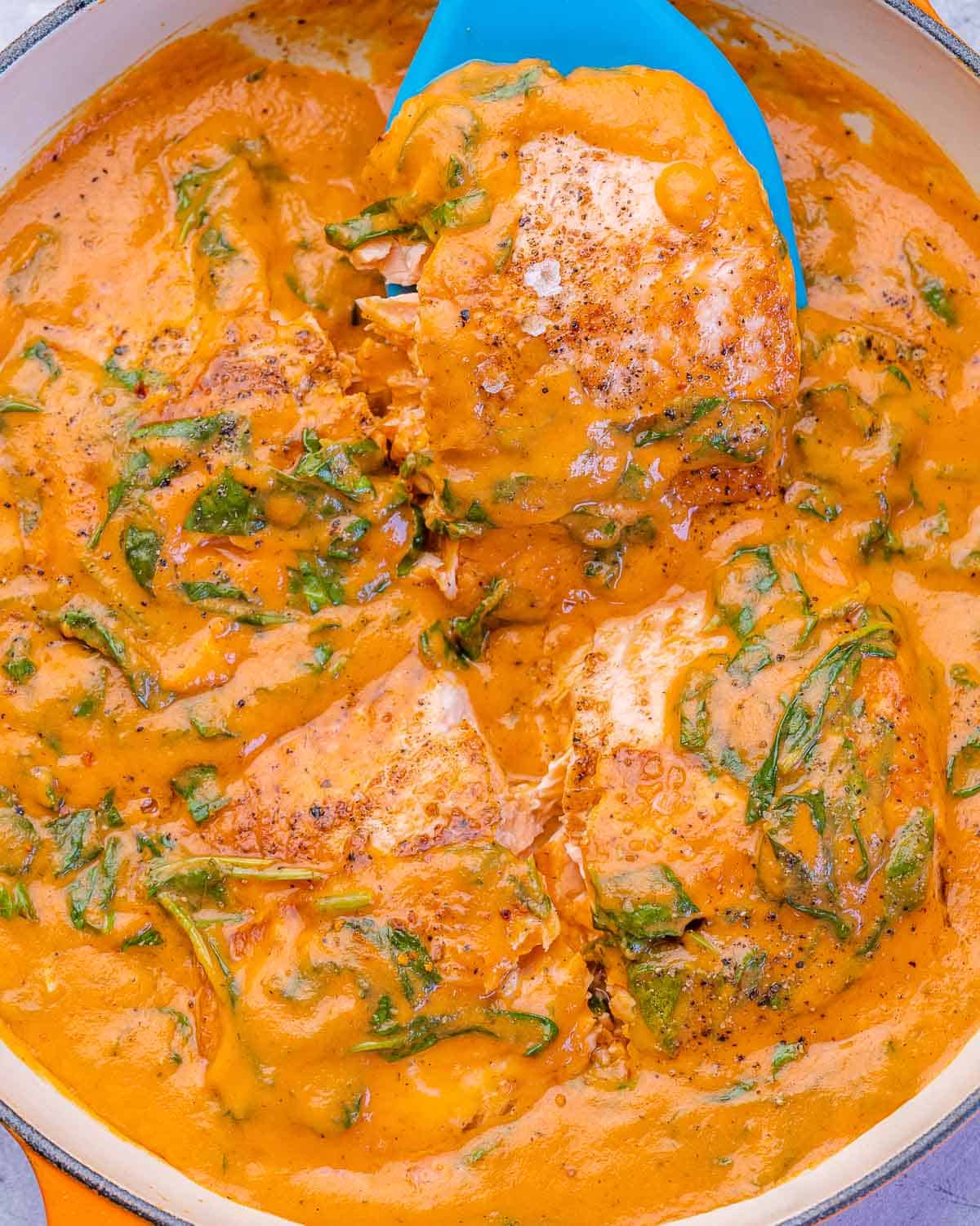 Close-up of salmon filets in a creamy spinach and roasted red pepper sauce, bubbling in a skillet.