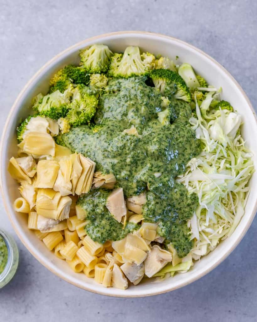 pesto added over a bowl of pasta, broccoli, shredded cabbage 