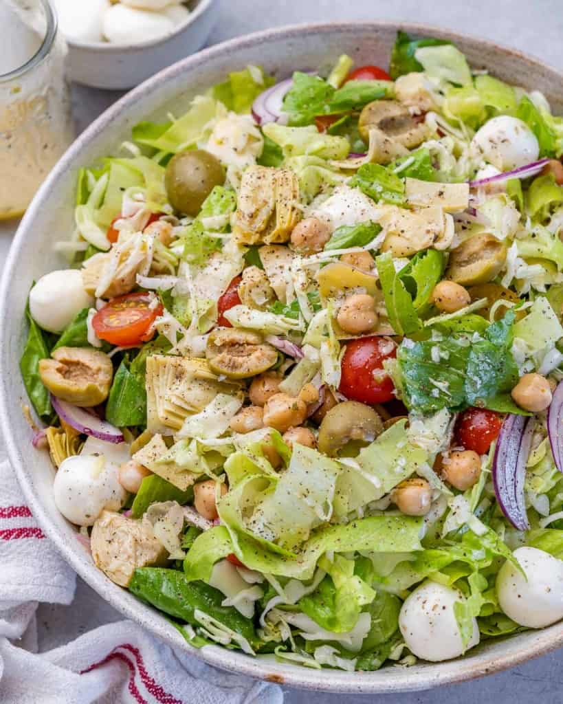 side shot of chopped salad on a bowl with mozzarella pearls olives, and artichoke