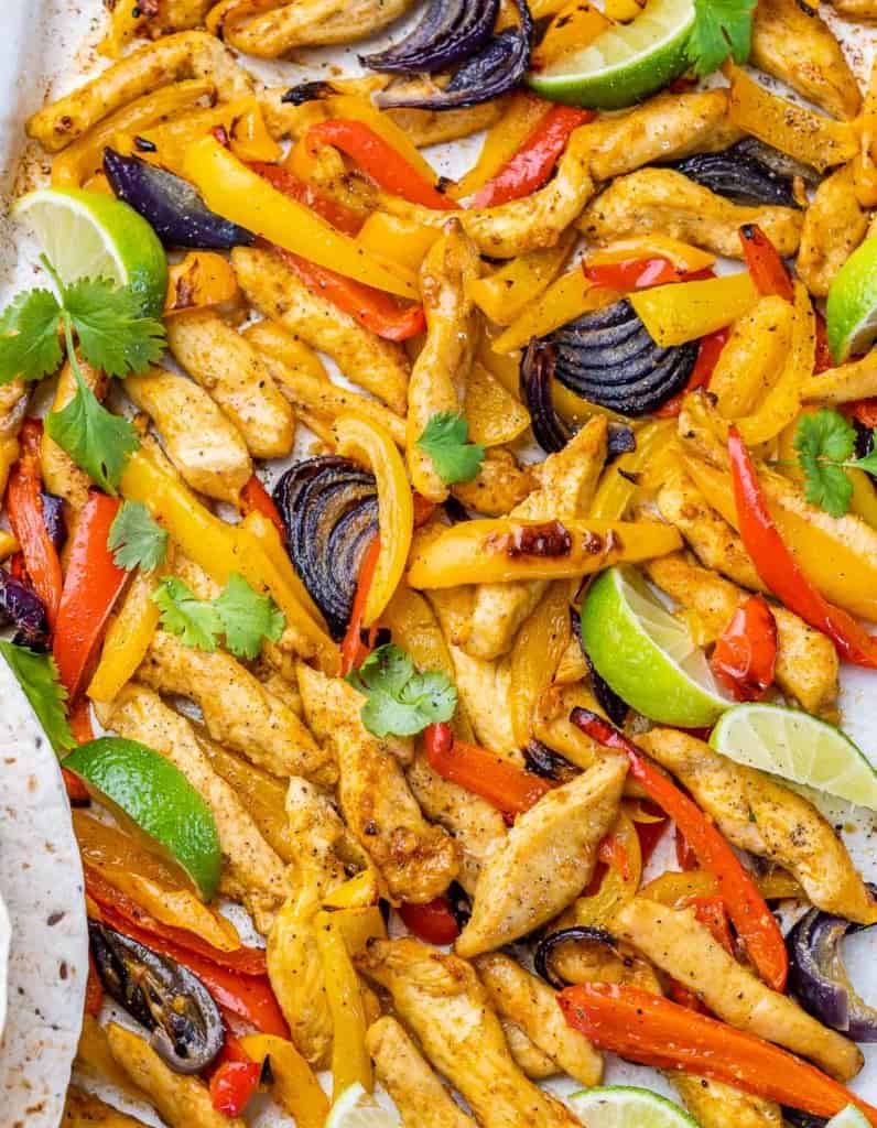 Chicken fajitas with bell peppers, onion and lime wedges on a sheet pan.
