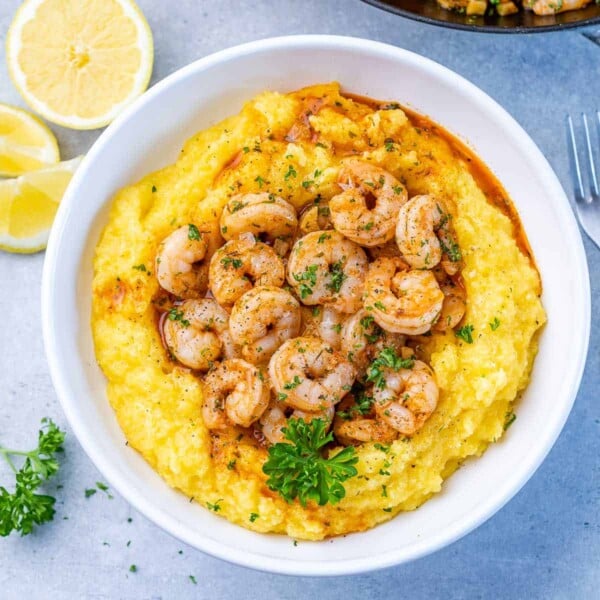 top view of yellow grits in a round white plate topped with sautéed shrimp