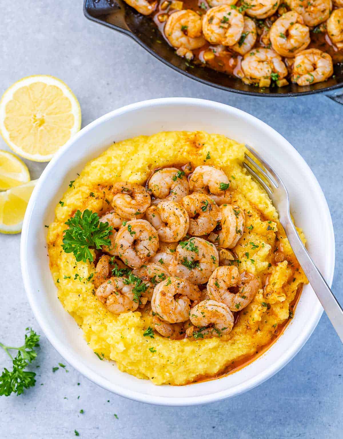 Top view of yellow grits in a round white plate topped with sautéed shrimp.