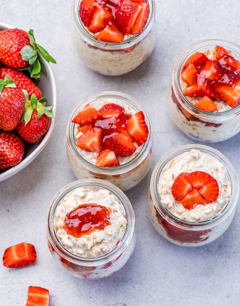 Assembling jars with overnight oats, strawberry preserves and fresh chopped strawberries.