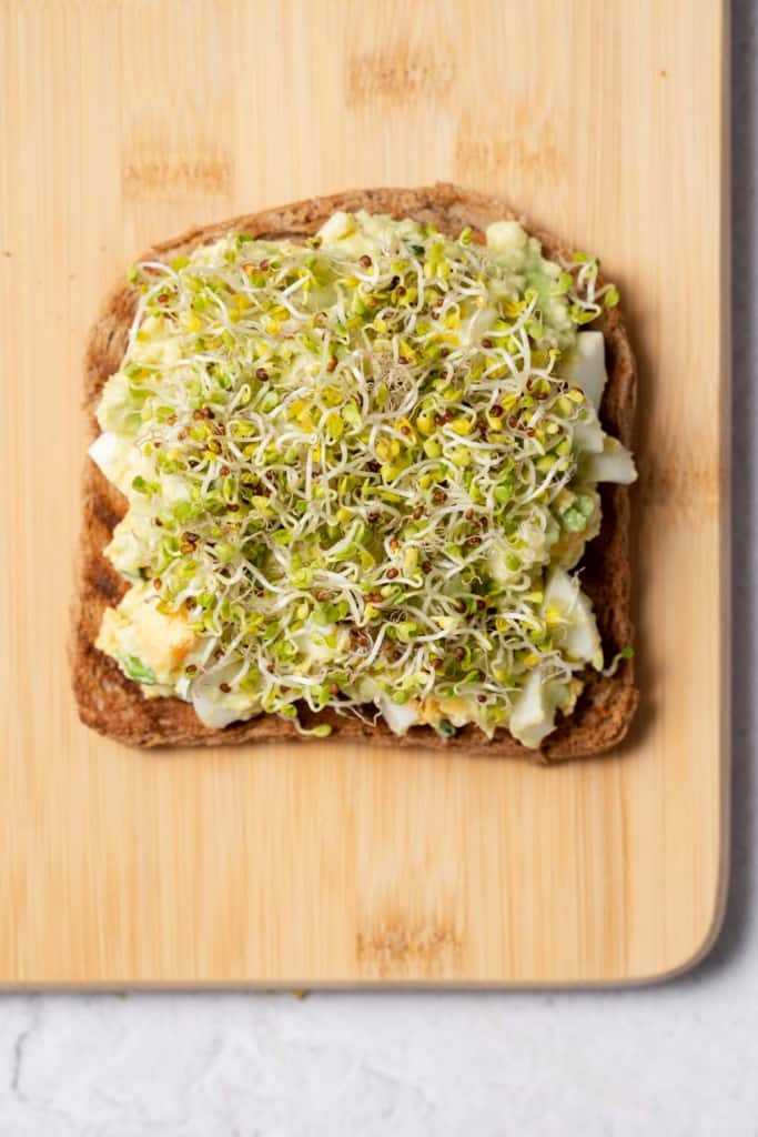 Topping egg salad on bread with sprouts.