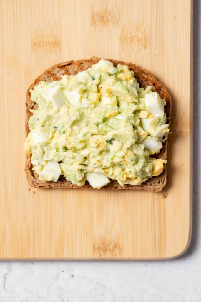 Adding egg salad to a slice of bread.