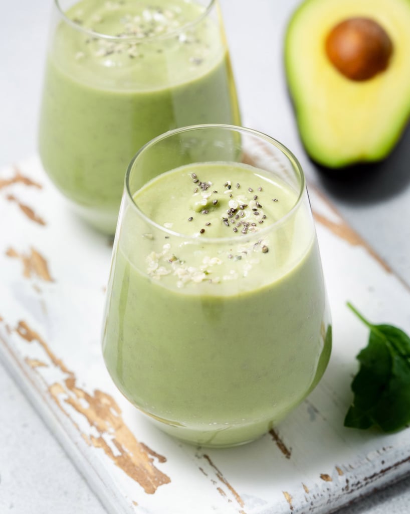 side shot of green avocado smoothie in a cup on a white cutting board