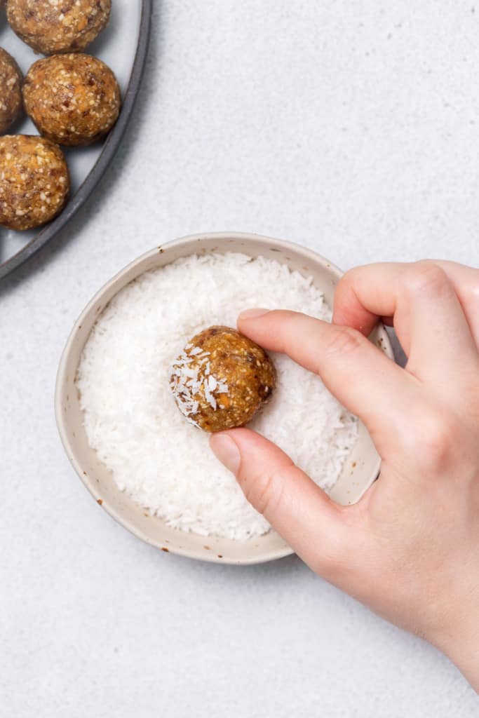 Rolling a carrot cake energy ball into shredded coconut.