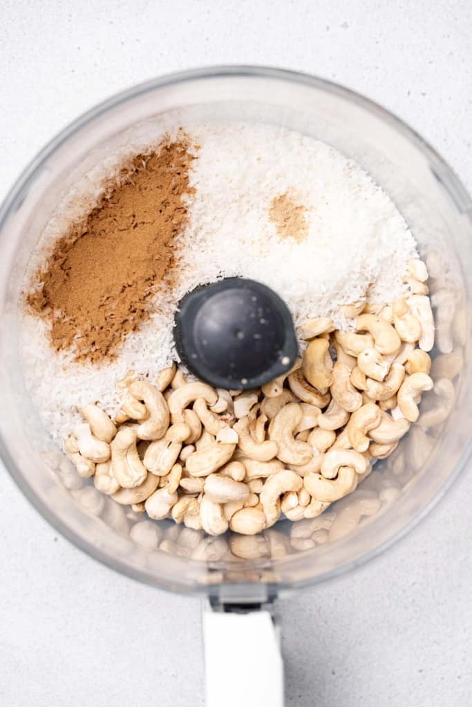 Adding cashews, spices and coconut to a food processor.