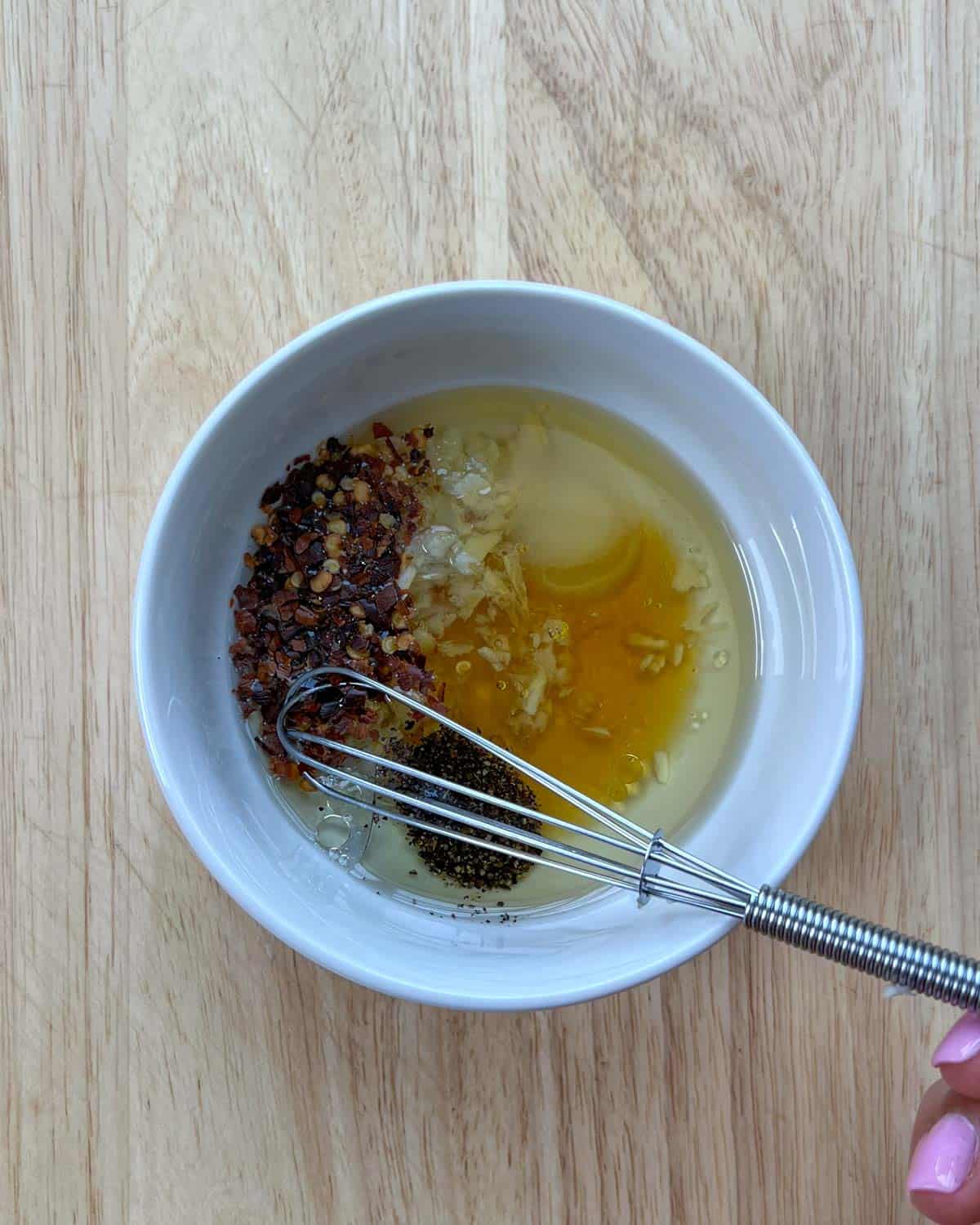 A bowl with dressing ingredients before mixing with a whisk.