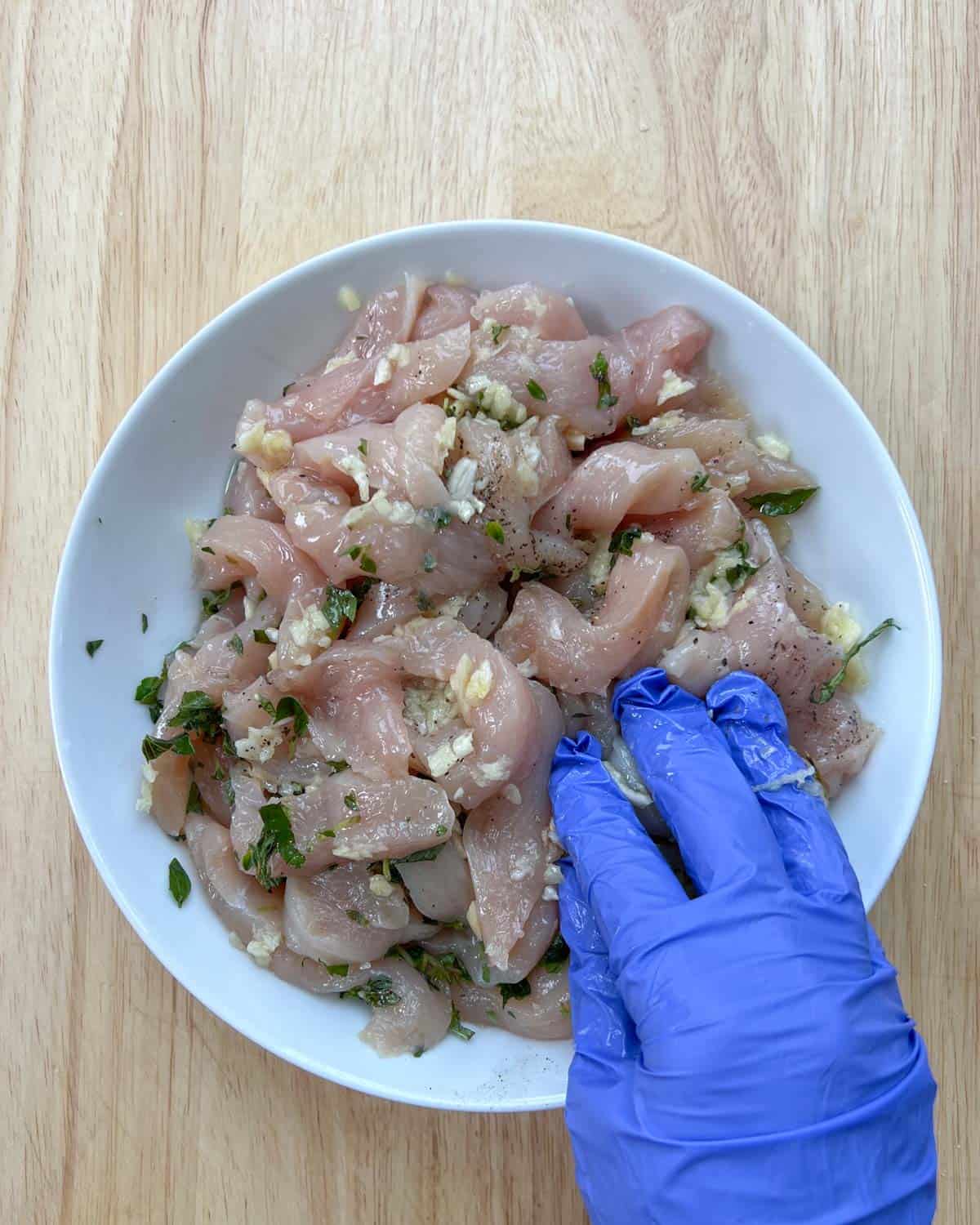 Hand mixing the chicken seasoning with chicken on a plate.