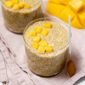 top side shot of a cup of orange color chia pudding in a cup topped with chopped mango