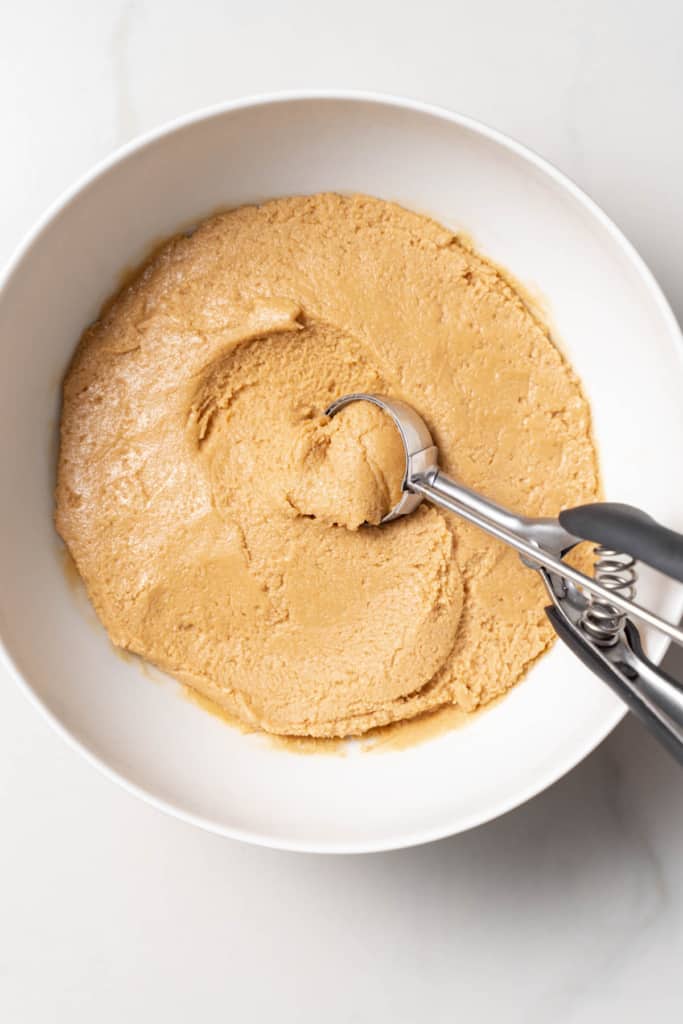 Scooping peanut butter dough out of a white bowl.