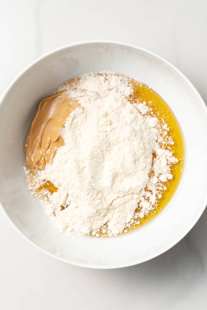 Adding coconut flour to a bowl with honey and peanut butter.
