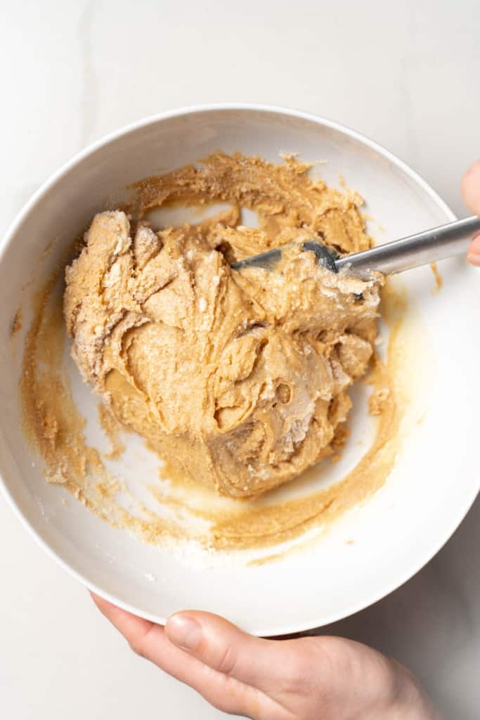 Stirring peanut butter, honey and coconut flour in a white bowl.