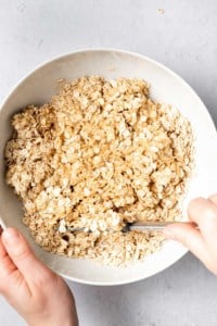 Using a spatula to stir oats into peanut butter and honey mixture.