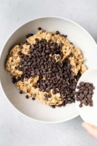 Pouring chocolate chips into a bowl with oat peanut butter mixture.