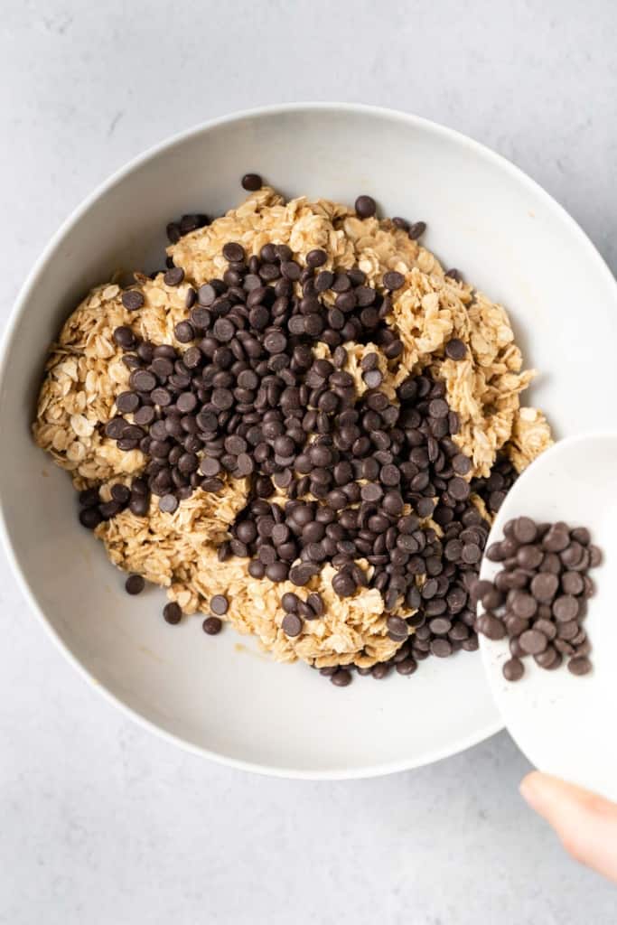 Pouring chocolate chips into a bowl with oat peanut butter mixture.