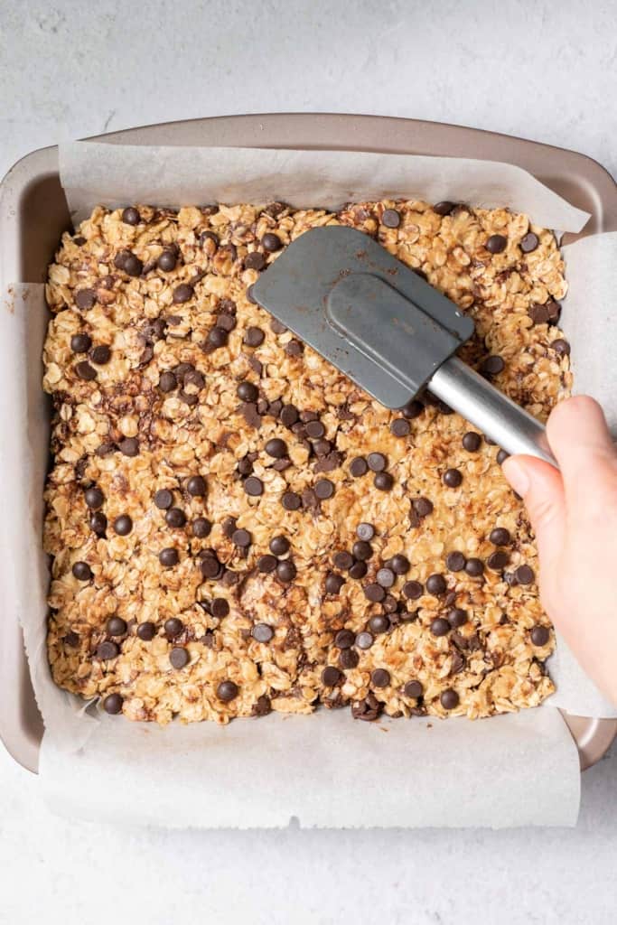Using a spatula to spread peanut butter oatmeal bar mixture in a pan.
