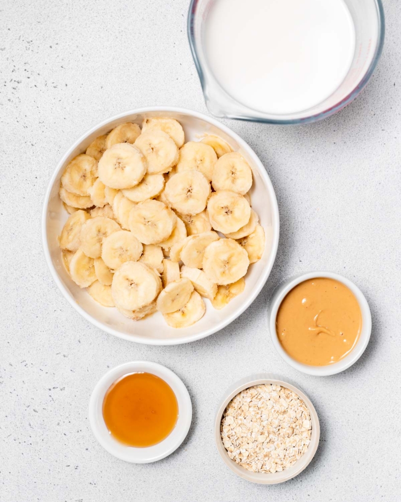 Milk, banana slices, peanut butter, honey and oats divided into bowls.