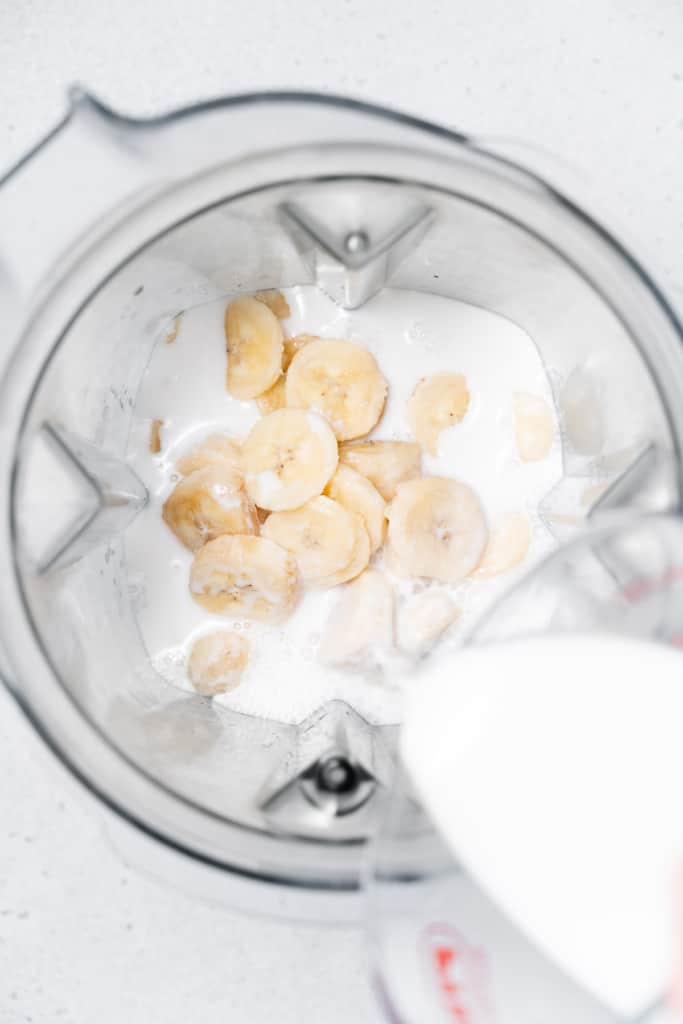 Pouring milk into blender with banana slices.