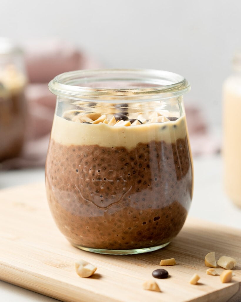 side shot of a jar with chocolate and peanut butter chia pudding on a cutting board