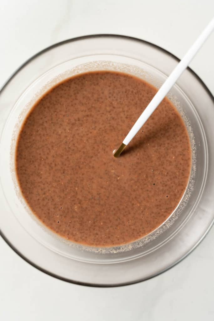 Stirring chia seeds with milk and cacao powder in a bowl.