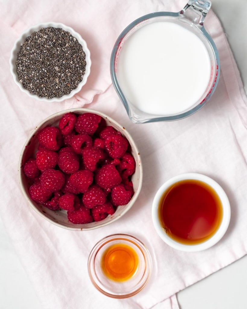 ingredients to make chia pudding: fresh raspberries, maple syrup, milk. chia seeds, and vanilla