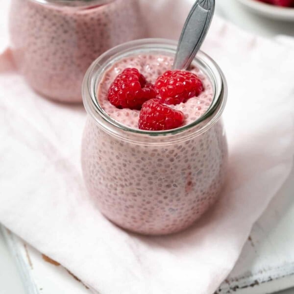 side shot of a jar of pink color chia pudding topped with fresh raspberry