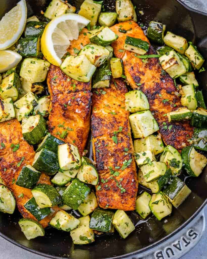 top view baked salmon with chopped zucchini on a black skillet