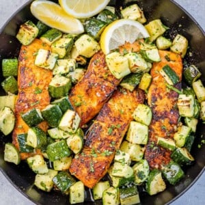 top view baked salmon with chopped zucchini on a black skilllet
