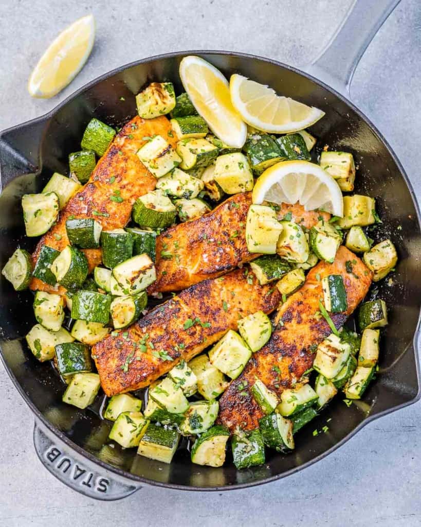 top view of 4 baked salmon filets with chopped zucchini on a pan 