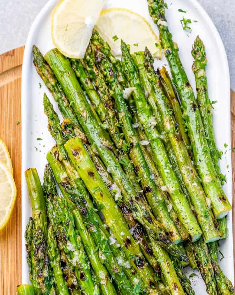 top view of grilled asparagus on a plate with lemon wedges on top side 