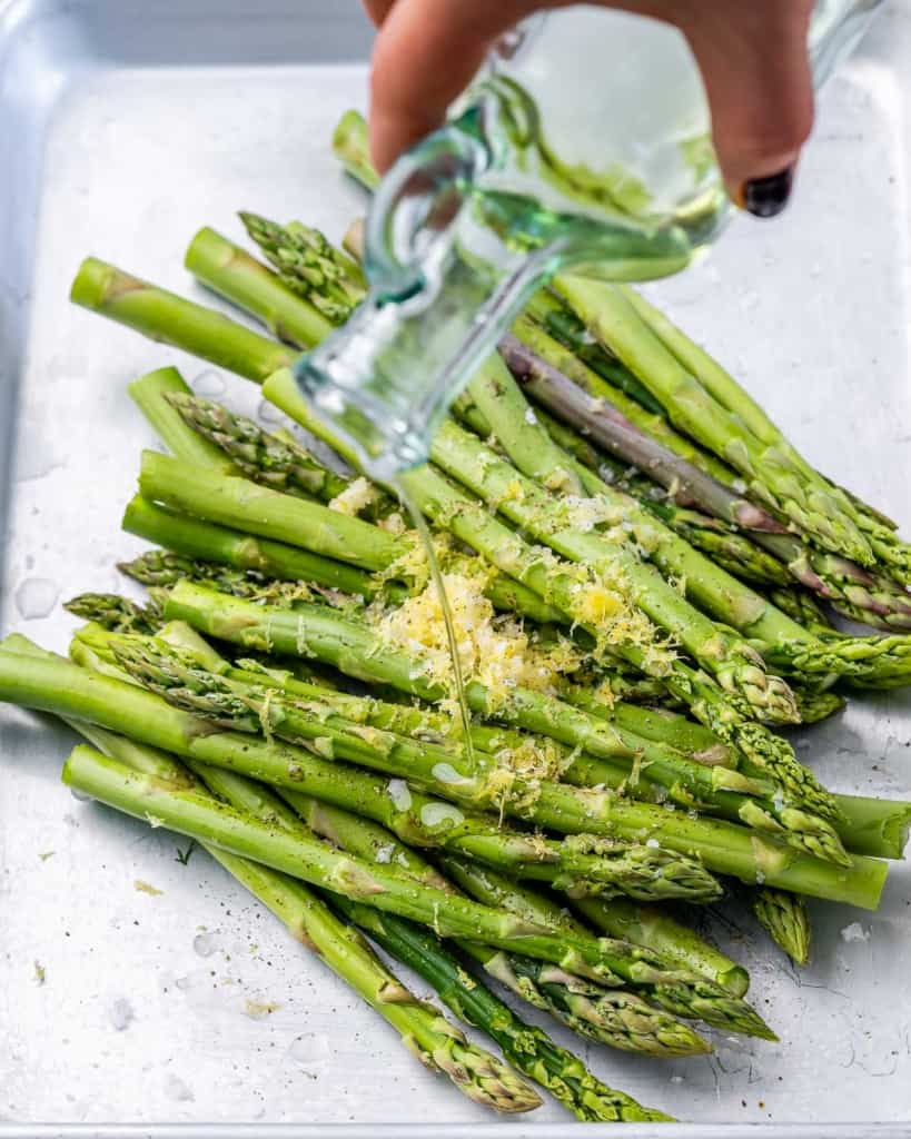 Drizzling olive oil over spears of asparagus.