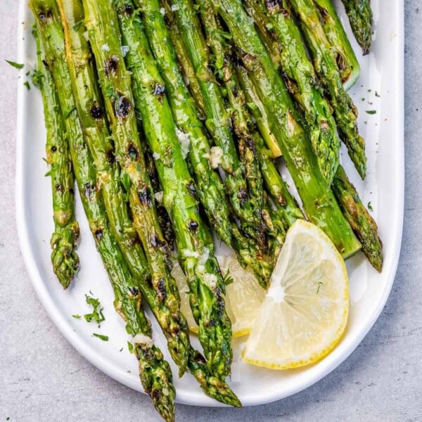 Top view grilled asparagus on white plate with lemon garnish.