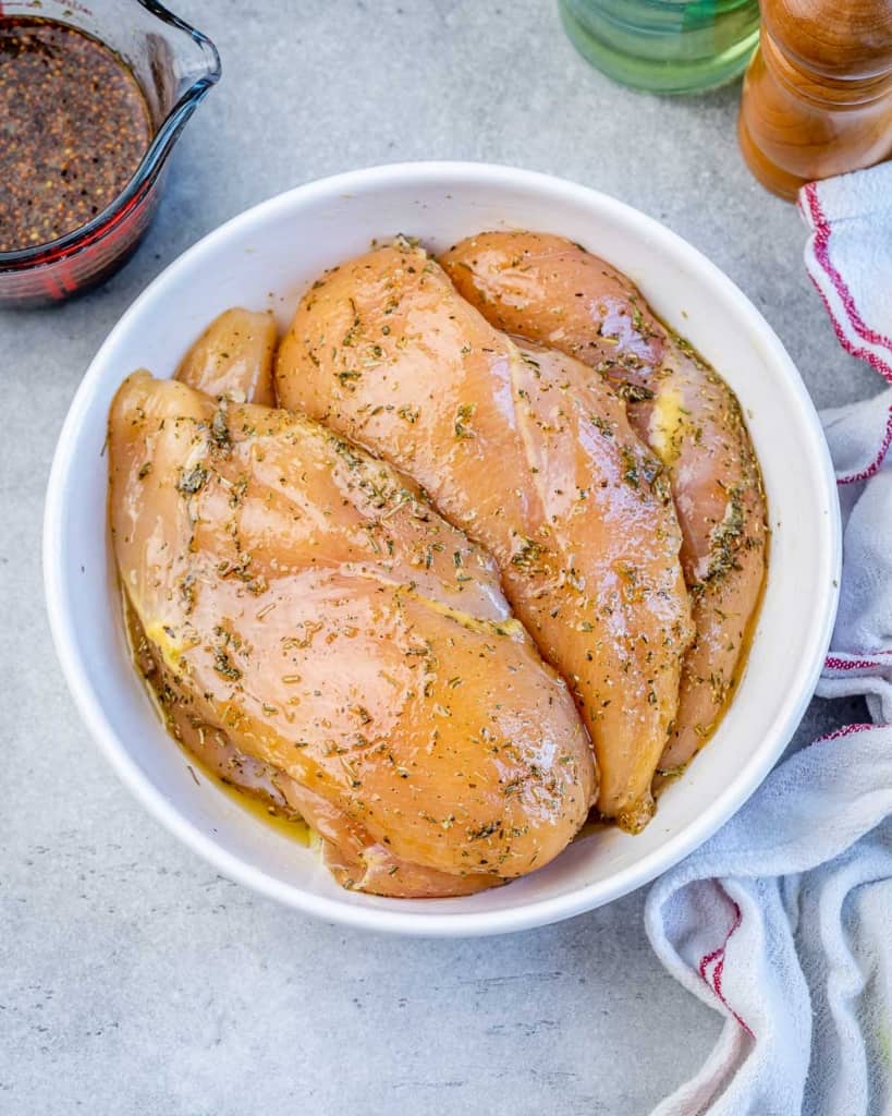 Seasoned chicken breasts in a white bowl.