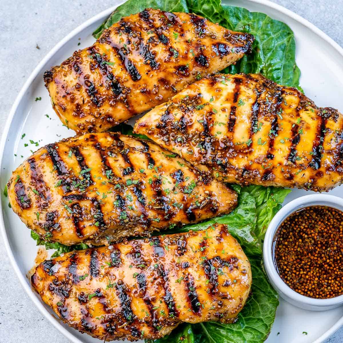 Top view of 4 grilled chicken breasts on a plate over a lettuce leaf.