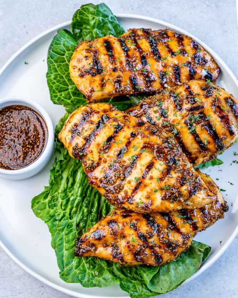 Top view of 4 grilled chicken breasts on a plate over a lettuce leaf.