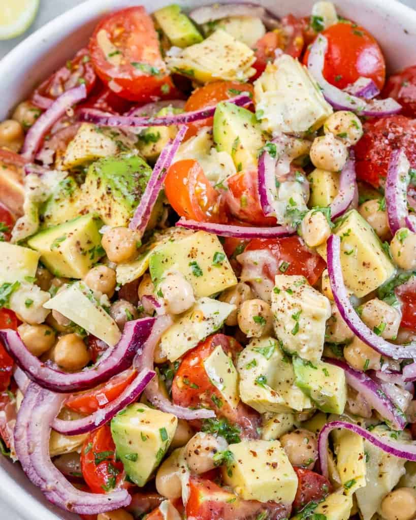 Closeup of a tomato salad tossed with artichokes, red onion and avocado.