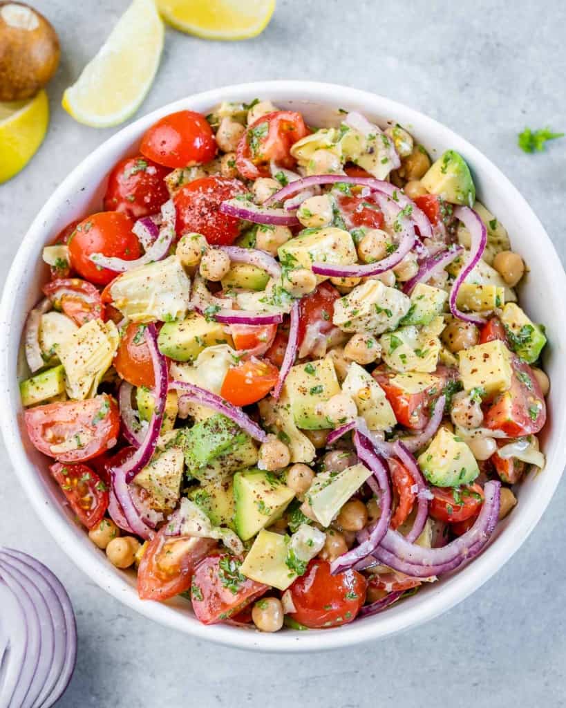 Top view salad with tomato, chickpea, onion and artichoke in a round white bowl.